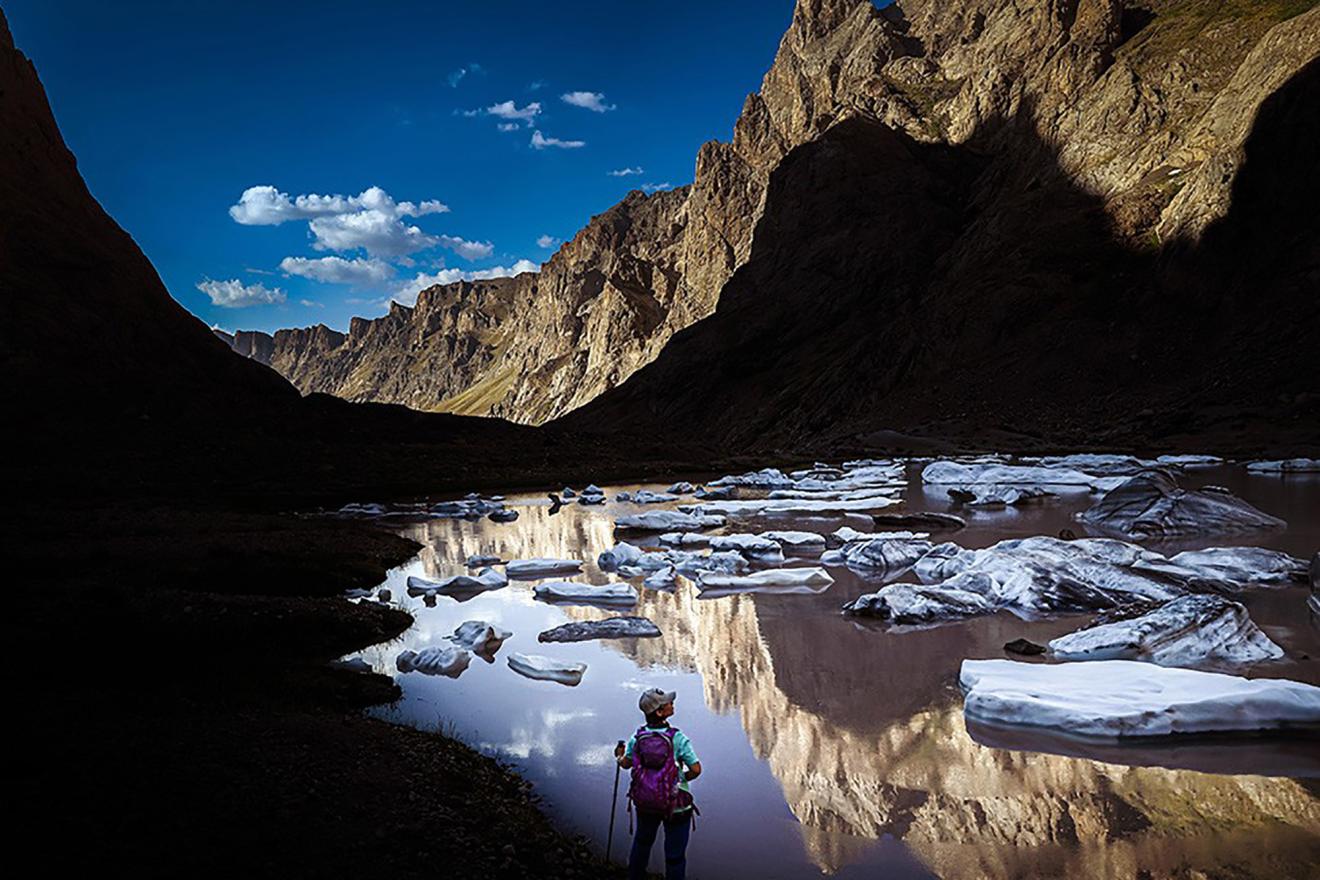A hiker standing near a body of water surrounded by rocky mountains.